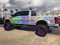 a silver truck parked in a parking lot next to other cars and trucks with purple rims