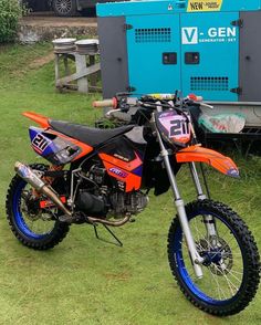 an orange dirt bike parked on top of a lush green field next to a blue trailer