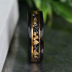 a black and gold wedding band with leaves inlayed to the side, sitting on a table next to a plant