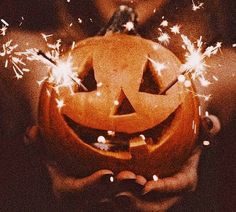 a person holding a pumpkin with sparklers in their hands