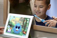 a young boy is playing with an electronic device while his mother watches from behind him