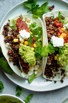 three tacos on a plate with guacamole, sour cream and cilantro