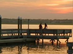 two people sitting on a dock at sunset