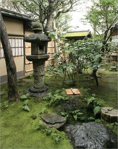 a stone lantern in the middle of a garden with moss growing on the ground and trees around it