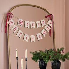 there is a christmas banner hanging on the wall next to two vases with candles