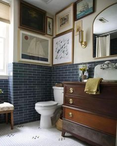 a white toilet sitting in a bathroom next to a wooden dresser with drawers and pictures on the wall