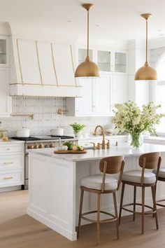 a large kitchen with white cabinets and gold pendant lights hanging over the island, along with four bar stools