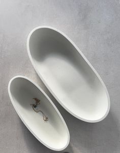 two white oval shaped dishes sitting on top of a gray tablecloth covered floor next to each other