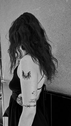 a woman with a tattoo on her arm standing in front of a wall and looking into the mirror