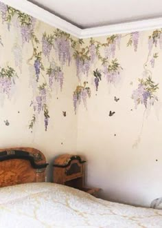 a bed sitting in a bedroom next to a wall with purple flowers hanging from it