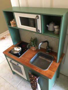 a green toy kitchen with sink, stove and microwave