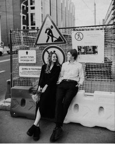 black and white photograph of two women sitting on the side of a road with construction signs behind them