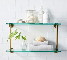 two glass shelves with towels, soaps and other items on them against a white brick wall