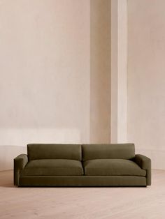 a green couch sitting on top of a hard wood floor next to a white wall