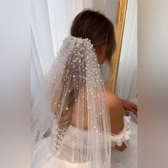 a woman in a wedding dress looking at herself in the mirror wearing a white veil