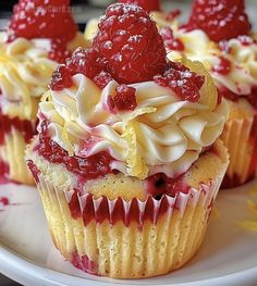 three cupcakes with raspberries and cream frosting on a white plate