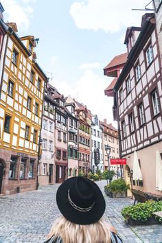 a woman wearing a black hat walking down a cobblestone street in an old european town