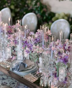 the table is set with silverware and purple flowers