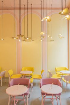 the interior of a restaurant with yellow and pink chairs, round tables and lamps hanging from the ceiling