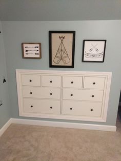 a white dresser sitting in the corner of a room next to pictures on the wall