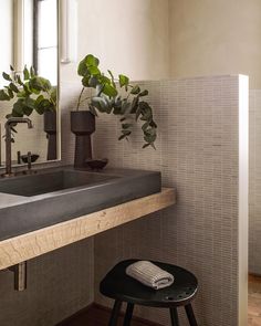 a bathroom sink sitting under a mirror next to a stool with a potted plant on it