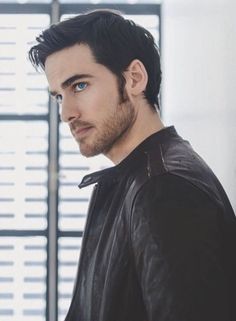 a man in a black leather jacket looking off into the distance with his hand on his hip