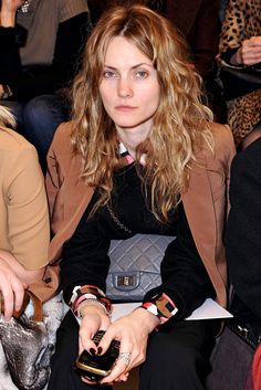 a woman sitting in the front row at a fashion show with her purse and cell phone