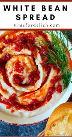 white bean spread with red sauce and herbs in the middle on a plate next to bread