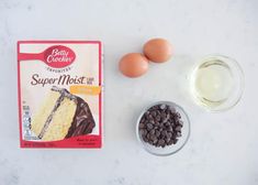 ingredients needed to make chocolate cake on a white counter top, including eggs and vanilla