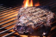 a steak is cooking on the grill with flames in the backgroung and it appears to be grilled