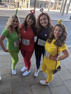 four women dressed in costumes posing for a photo on the sidewalk with one woman wearing a costume