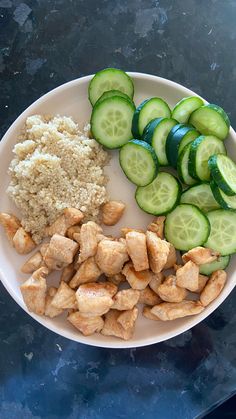 a white plate topped with cucumbers and chicken next to rice on top of a table