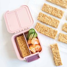 an open lunch box with crackers and fruit in it on a white surface next to other food items