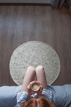 a woman is sitting on the floor with her feet up and holding a cup of coffee