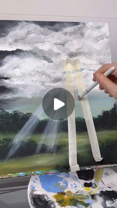 someone is painting a landscape with clouds and sun beams in the sky on an easel