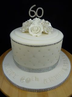 a white cake with flowers and the number sixty on top is sitting on a wooden table