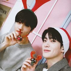 two young men wearing christmas hats and holding candy lollipops in their hands