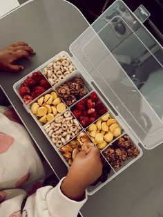 a child reaching for nuts in a plastic container on a table with text overlay that reads, she thoroughly enjoy the snack box made her although most of