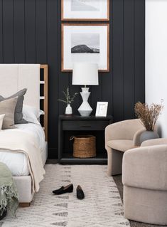 a bedroom with black walls and white bedding, two armchairs and a rug on the floor