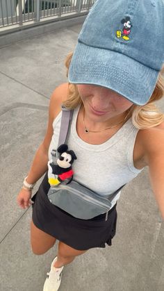 a girl wearing a mickey mouse hat and carrying a bag with a stuffed animal in it