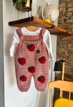 a baby's strawberry knitted outfit hanging on a clothesline next to a chair