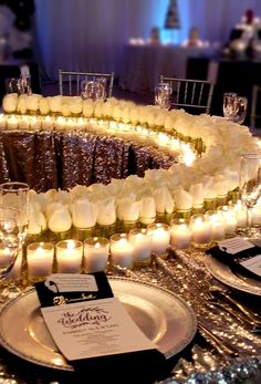 a table topped with lots of white roses next to glasses and plates covered in candles