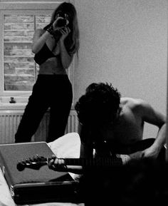 two people in a bedroom with one playing the guitar