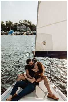 a man and woman sitting on the back of a sailboat in front of a body of water