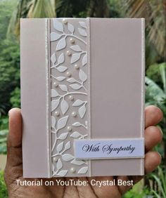 a hand holding up a card that is decorated with leaves and pearls on the front