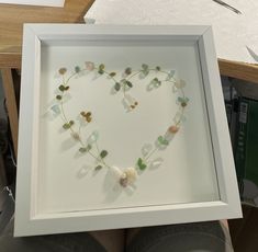 a heart shaped frame with sea glass and flowers in the shape of a heart on it