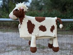 a crocheted cow is hanging on a fence