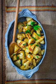 a blue bowl filled with cooked potatoes on top of a wooden table next to a spoon