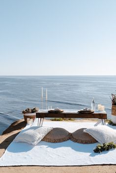 a table with pillows and plates on it near the ocean