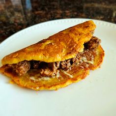 a piece of food on a white plate with meat and cheese in the middle, sitting on a granite counter top